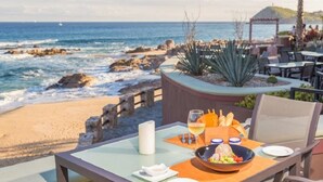 Mesa preparada para comer con vista al océano, una planta y un pabellón de jardín al fondo.