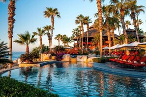 A resort pool area with palm trees, lounge chairs, and a building with a thatched roof.
