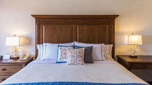 Habitación de hotel con una cama grande, cabecera de madera, dos mesitas de noche con lámparas y almohadones decorativos.