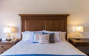 A hotel room with a large bed, wooden headboard, two bedside tables with lamps, and decorative pillows.