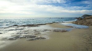 Una playa con arena, olas y un promontorio rocoso a lo lejos.