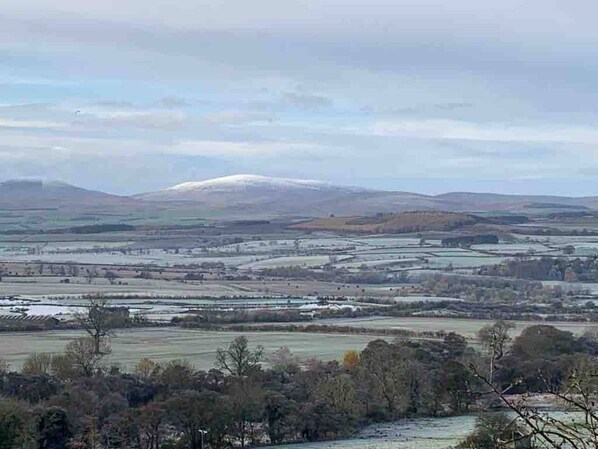 A panoramic view of a rural landscape with fields, a distant mountain, and a small settlement. - Rural Oasis in the heart of Northumberland (Belford)