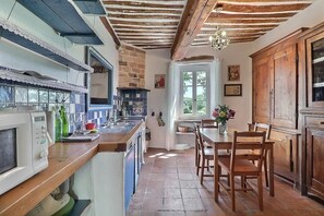 Une cuisine avec une table et des chaises en bois, une fenêtre et une porte qui donne sur une autre pièce.
