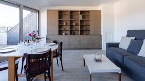 Ein modernes Wohnzimmer mit einer grauen Couch, einem Esstisch für vier Personen und einer eingebauten Regaleinheit mit verschiedenen Dekorationsgegenständen.