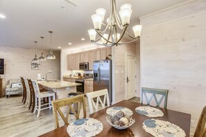 A modern kitchen with wooden cabinets, stainless steel appliances, and a dining area with a wooden table and chairs. - Hammock Dunes K | BIG Dogs | Beach Side | Pool | Free Parking | Beach Getaways (Orange Beach)