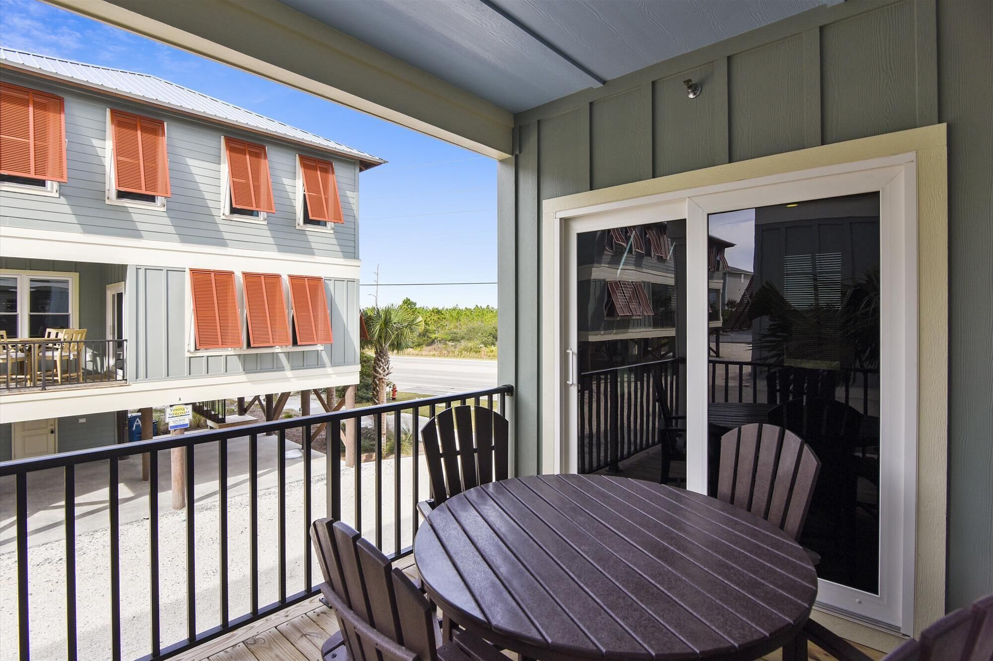 A balcony with a table and chairs, a view of a house with orange shutters, and a clear sky.