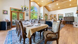 Une salle à manger spacieuse avec un plafond haut, des poutres en bois et de grandes fenêtres donnant sur l’extérieur.