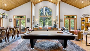 Une pièce spacieuse avec une table de billard, un plafond en bois, de grandes fenêtres et un coin salon confortable.