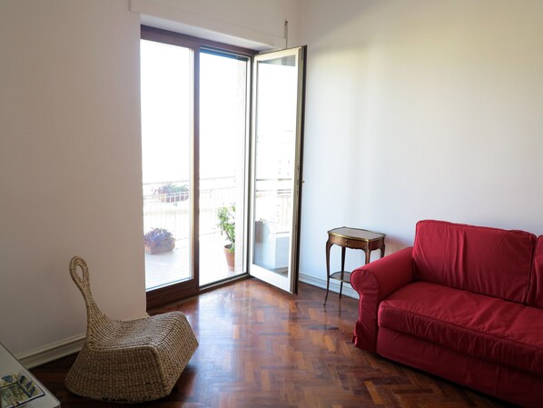 Une pièce avec un canapé rouge, un fauteuil en osier et une petite table en bois.