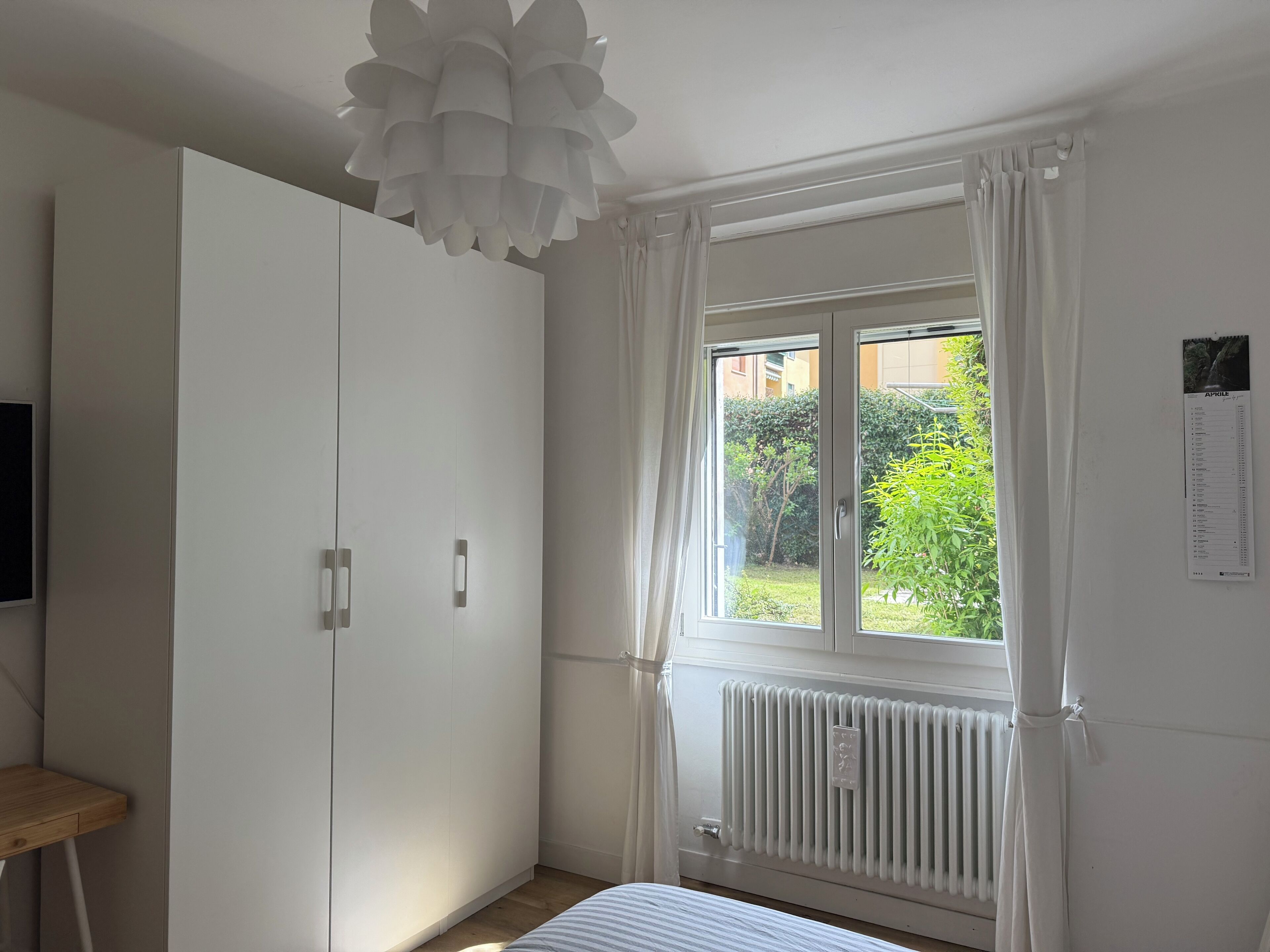 Une chambre avec une grande armoire, une fenêtre avec des rideaux, un radiateur et un lit.