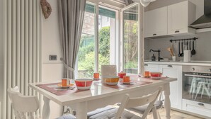 A bright kitchen with white cabinets, a dining table with chairs, and a view of greenery outside. - The Angolino apartment (TN)