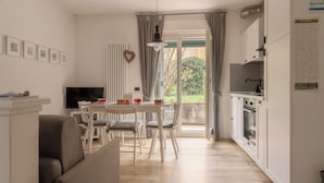 A modern kitchen with white cabinets, a dining area with a round table and chairs, and a television on a stand. - The Angolino apartment (TN)