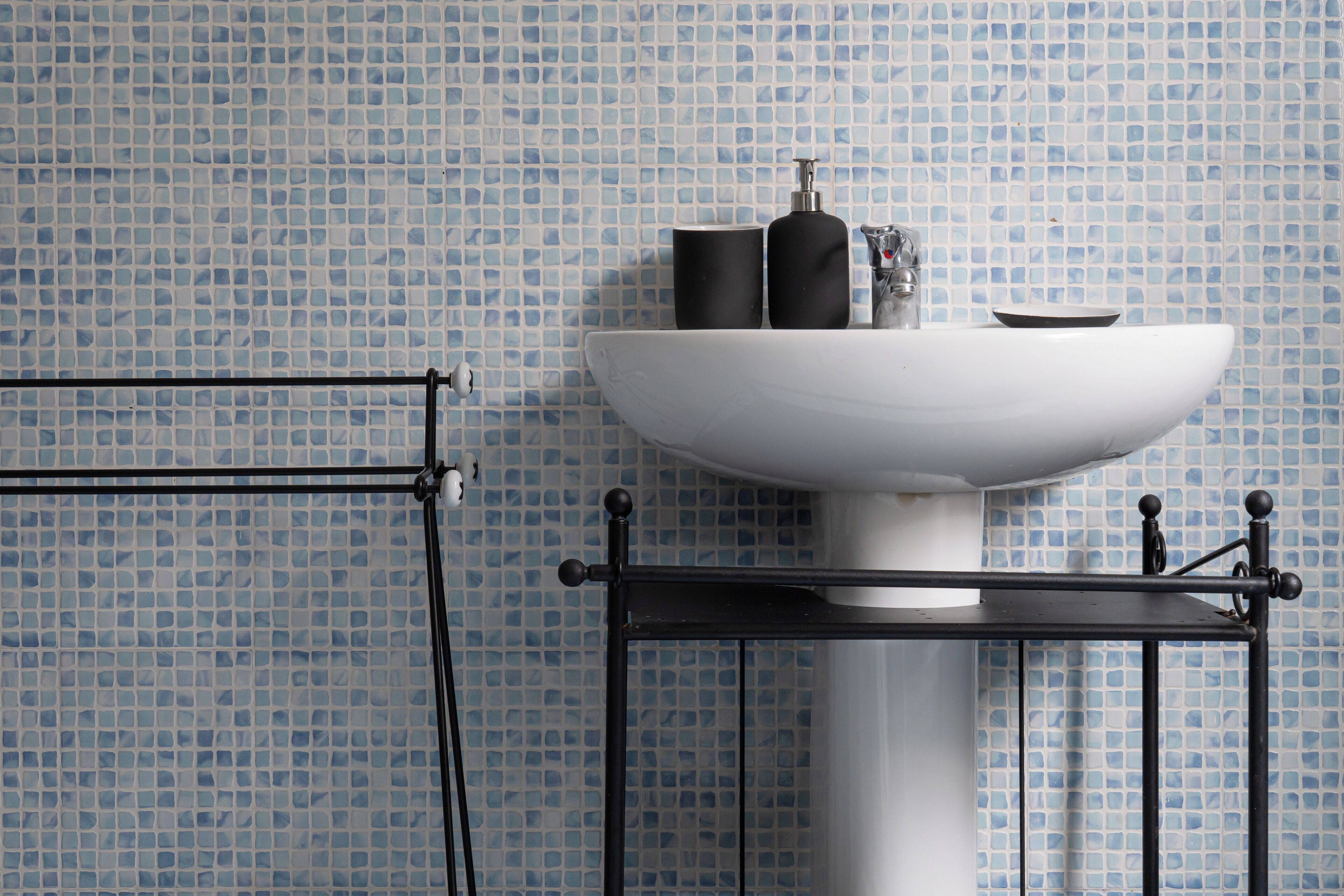 A bathroom with a white sink, black soap dispensers, and a black metal shelf.