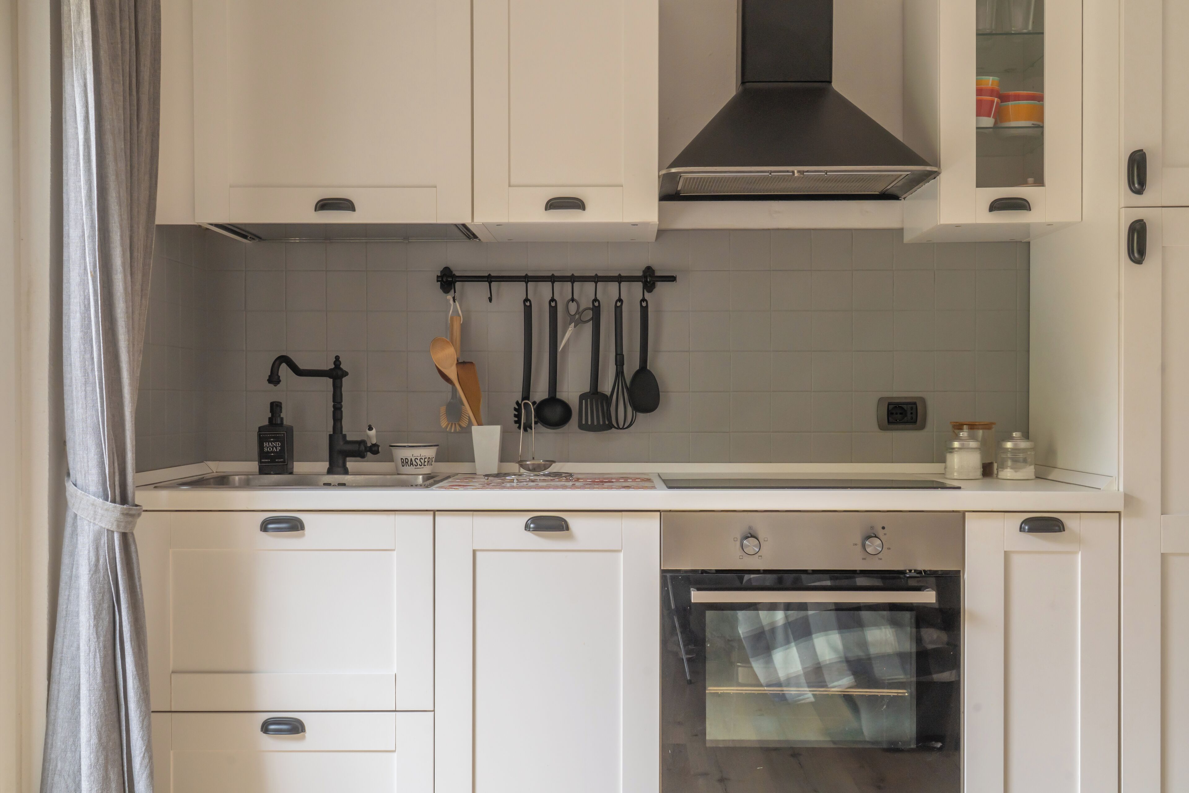 A compact kitchen with white cabinets, a built-in oven, and a hanging utensil rack.
