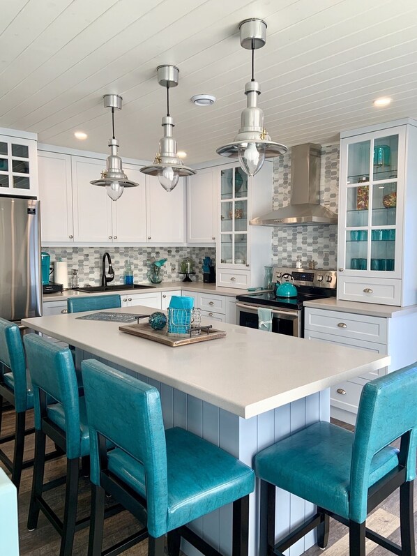 A modern kitchen with white cabinets, a large island with bar stools, stainless steel appliances, and pendant lighting.