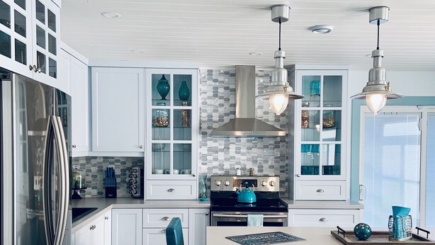 Une cuisine moderne avec des meubles blancs, un réfrigérateur en acier inoxydable, une bouilloire bleue et un coin repas avec des chaises bleues.