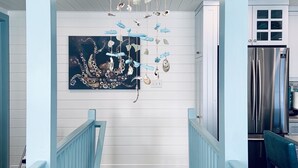 Un escalier avec des rampes bleu clair menant à une cuisine dotée de meubles blancs et d’un réfrigérateur en acier inoxydable.
