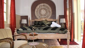 A traditional room with a bed, two bedside tables, a chair, a decorative wall piece, and a patterned rug. - Riad la medersa in Marrakesch (Marrakech)