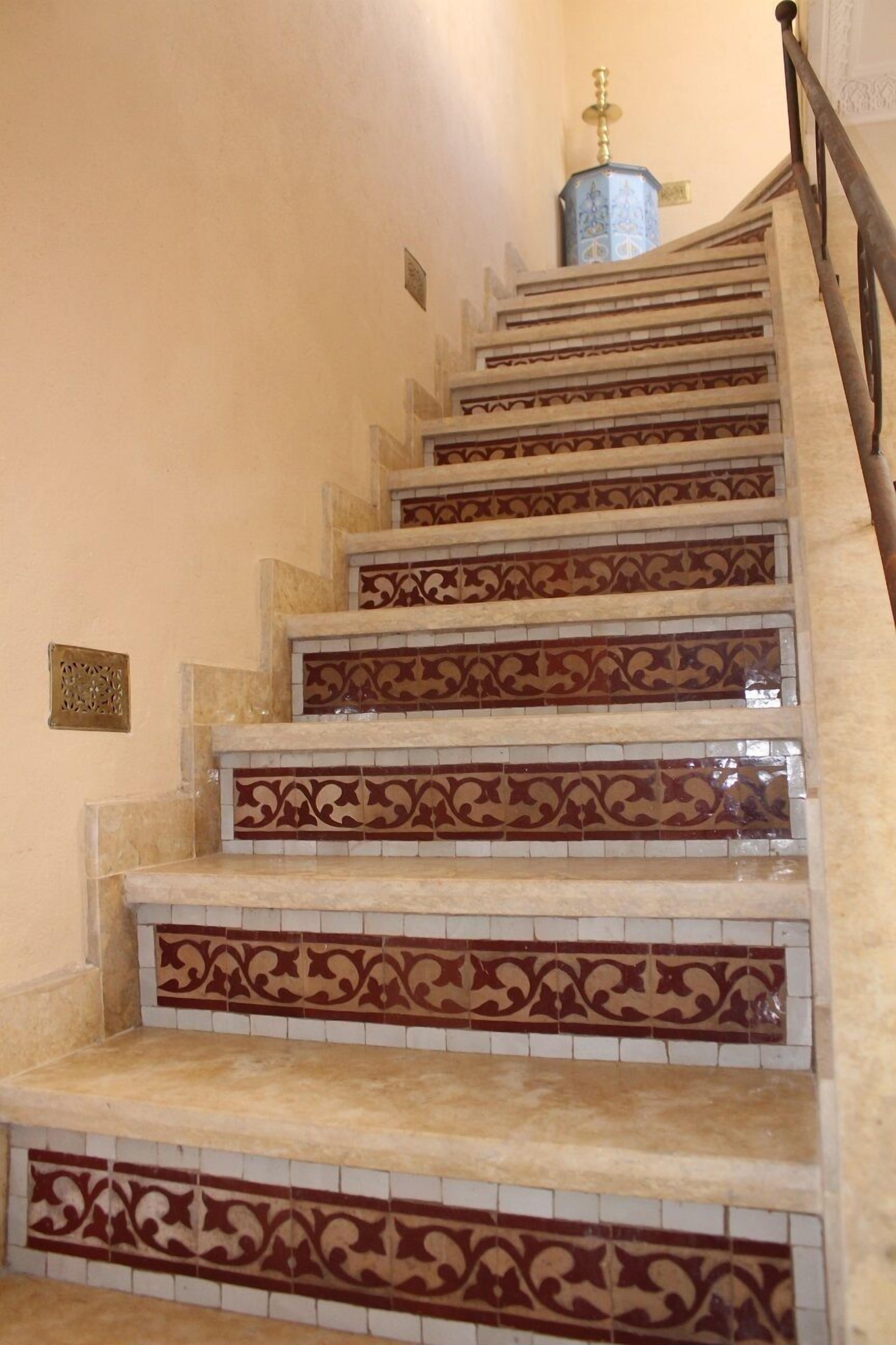Una escalera con intrincados diseños de baldosas rojas y blancas, y un objeto decorativo azul en la parte superior.