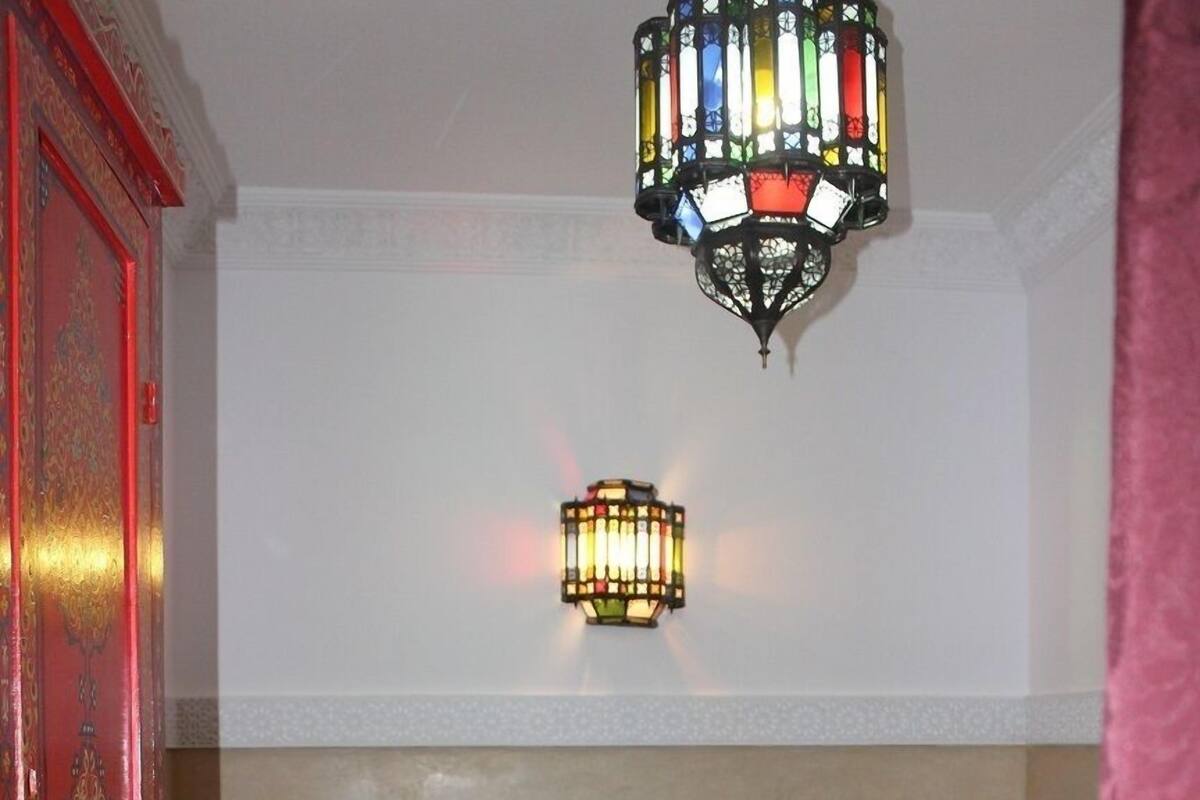 A bedroom with a bed, a red door, a chandelier, and two wall-mounted lanterns.