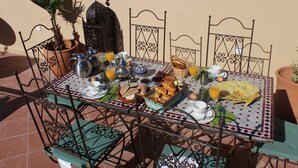 A breakfast table set with various dishes, including croissants, bread, and a plate of eggs, surrounded by metal chairs and a decorative lantern. - Riad la medersa in Marrakesch (Marrakech)