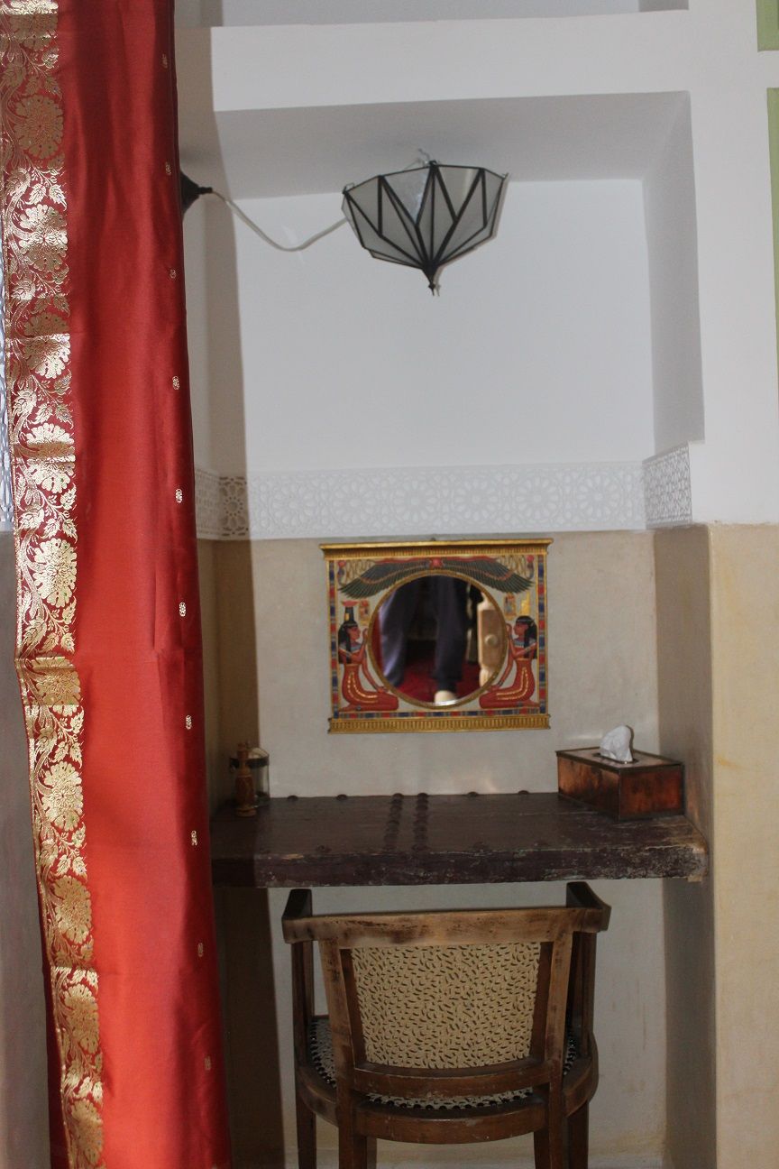 A room with a wooden table, a chair, a wall-mounted mirror, and a decorative lamp.
