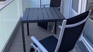 Ein Balkon mit Tisch und zwei Stühlen, einer Glastrennwand und Blick auf angrenzende Gebäude.