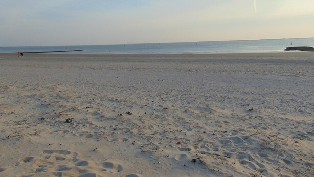 Ein weiter Sandstrand mit Fußabdrücken und einem entfernten Leuchtturm.
