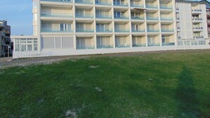 Ein mehrstöckiges Hotel mit Balkonen, einem weißen Zaun und einer Rasenfläche davor.