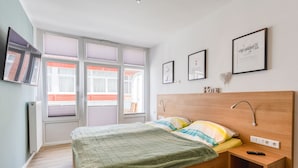 Ein Schlafzimmer mit Bett, Nachttisch und Fenster mit Jalousien. An der Wand hängen gerahmte Bilder.