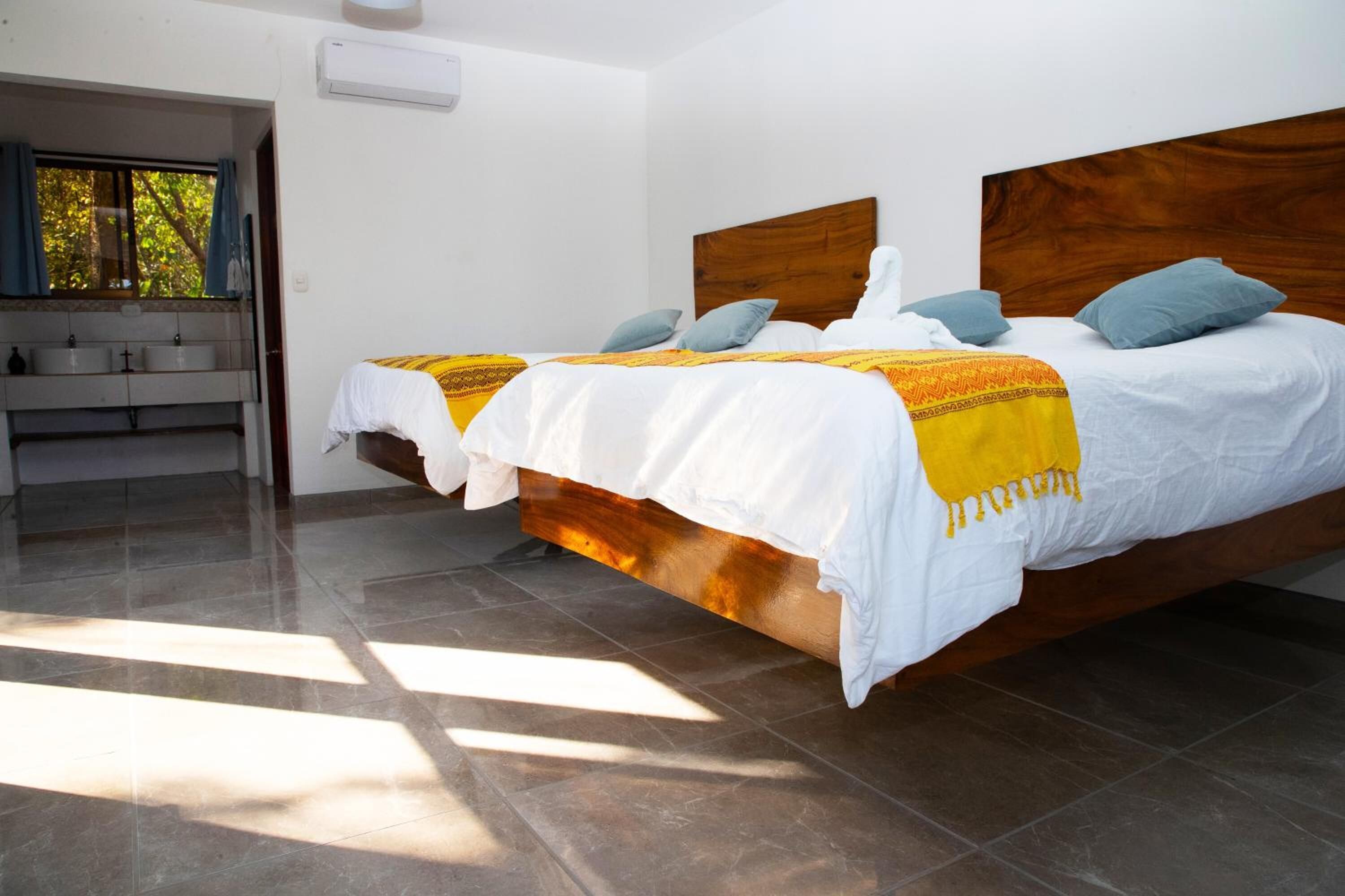 Una habitación de hotel con dos camas, un baño con lavamanos y una ventana con cortinas.