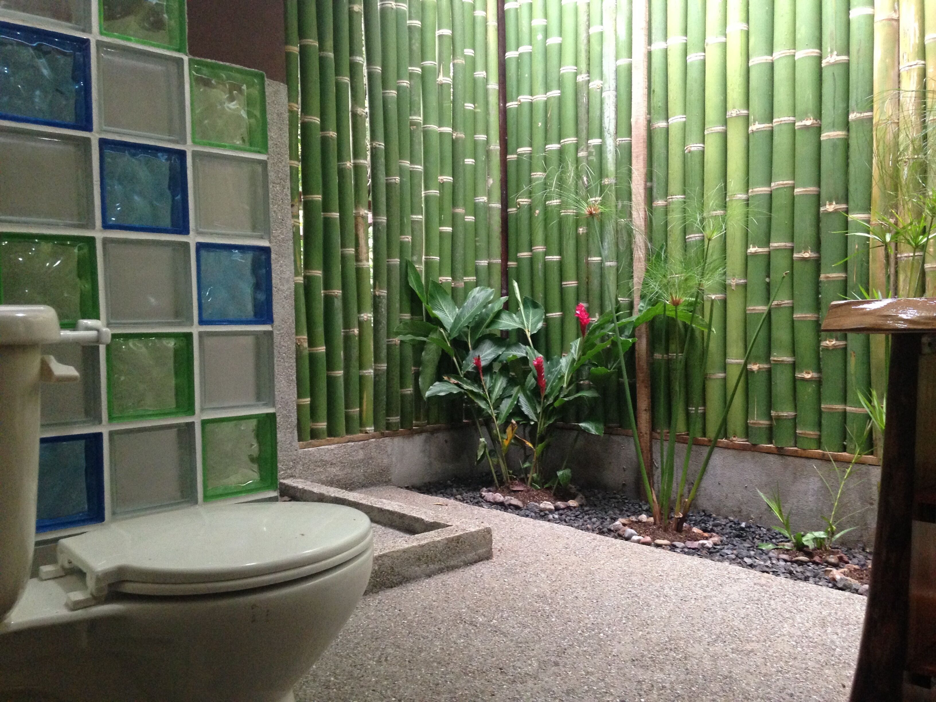A bathroom with a toilet, a green bamboo wall, and a tiled shower area.
