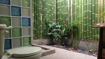 A bathroom with a toilet, a green bamboo wall, and a tiled shower area.