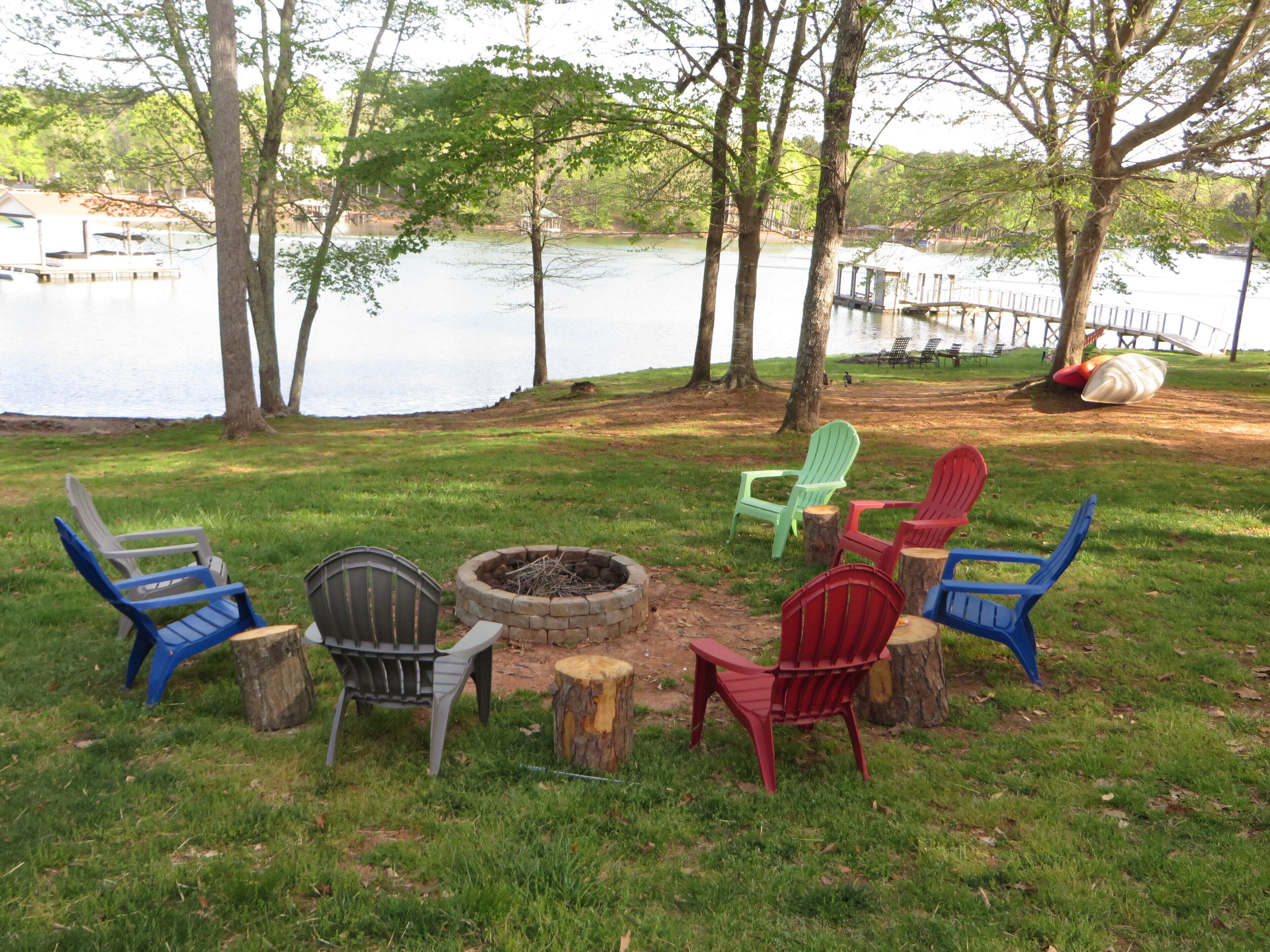 A lakeside seating area with Adirondack chairs and a fire pit.