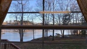 A view through a window with a view of a lake, trees, and a dock with chairs and a table. - Charming 3BR 2BA Lakefront Lake Norman Home with Beach & Dock - Sleeps 10 (Sherrills Ford)