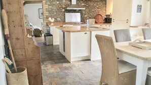 Una cucina con mobili bianchi, un muro in pietra e un soffitto in legno.