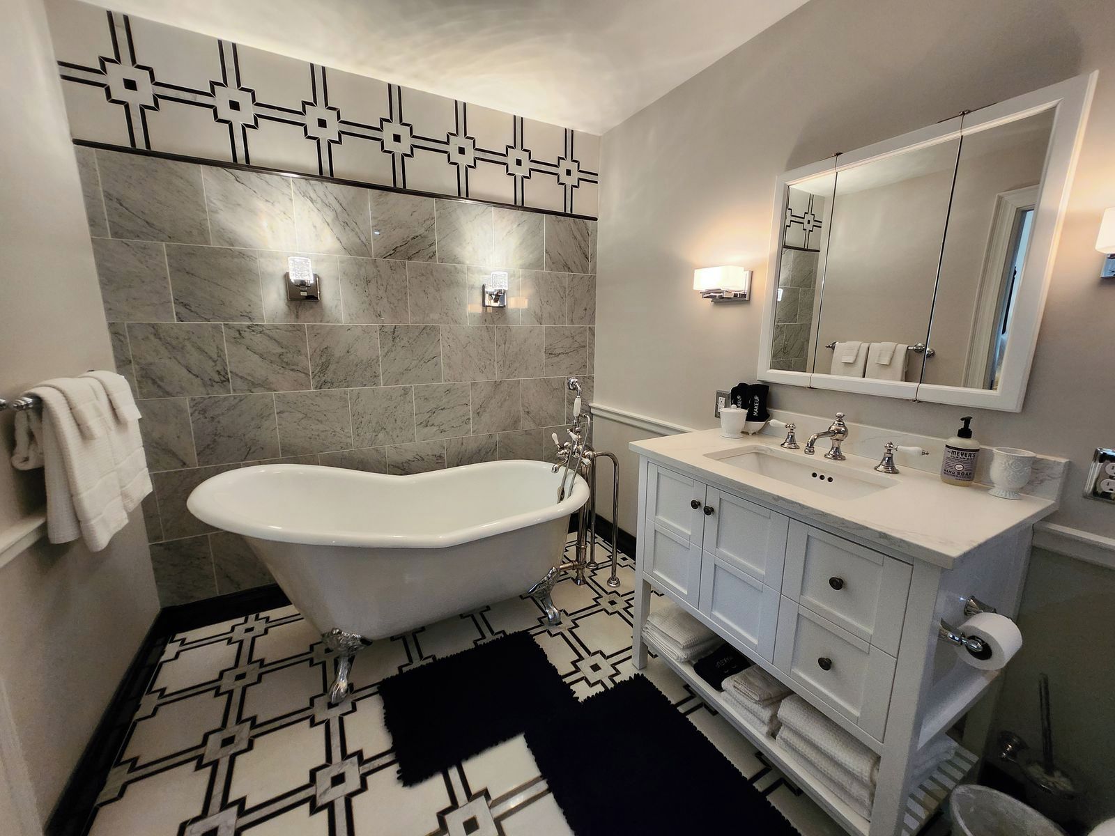 Une salle de bain avec une baignoire sur pieds, un meuble-lavabo avec un miroir et un carrelage décoratif.