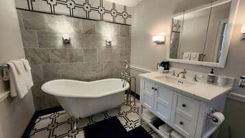 Une salle de bain avec une baignoire sur pieds, un meuble-lavabo avec un miroir et un carrelage décoratif.