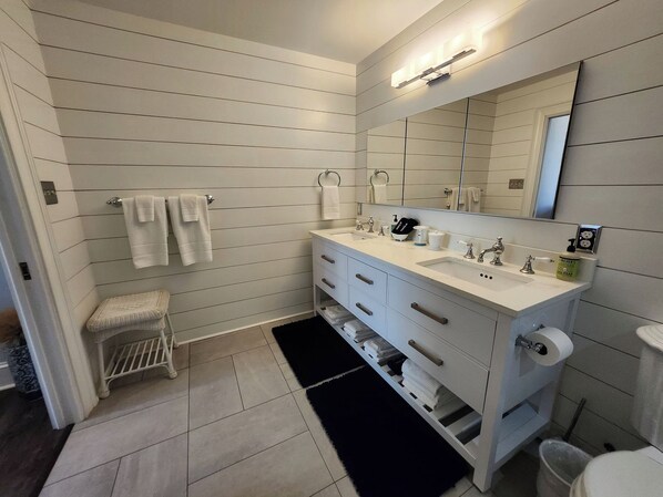 A modern bathroom with a white vanity, a large mirror, and a black rug. - Carriage House | River Views & Pool (New Kent)