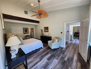 A bedroom with a bed, a chair, a desk, a ceiling fan, and a door leading to another room. - Carriage House | River Views & Pool (New Kent)