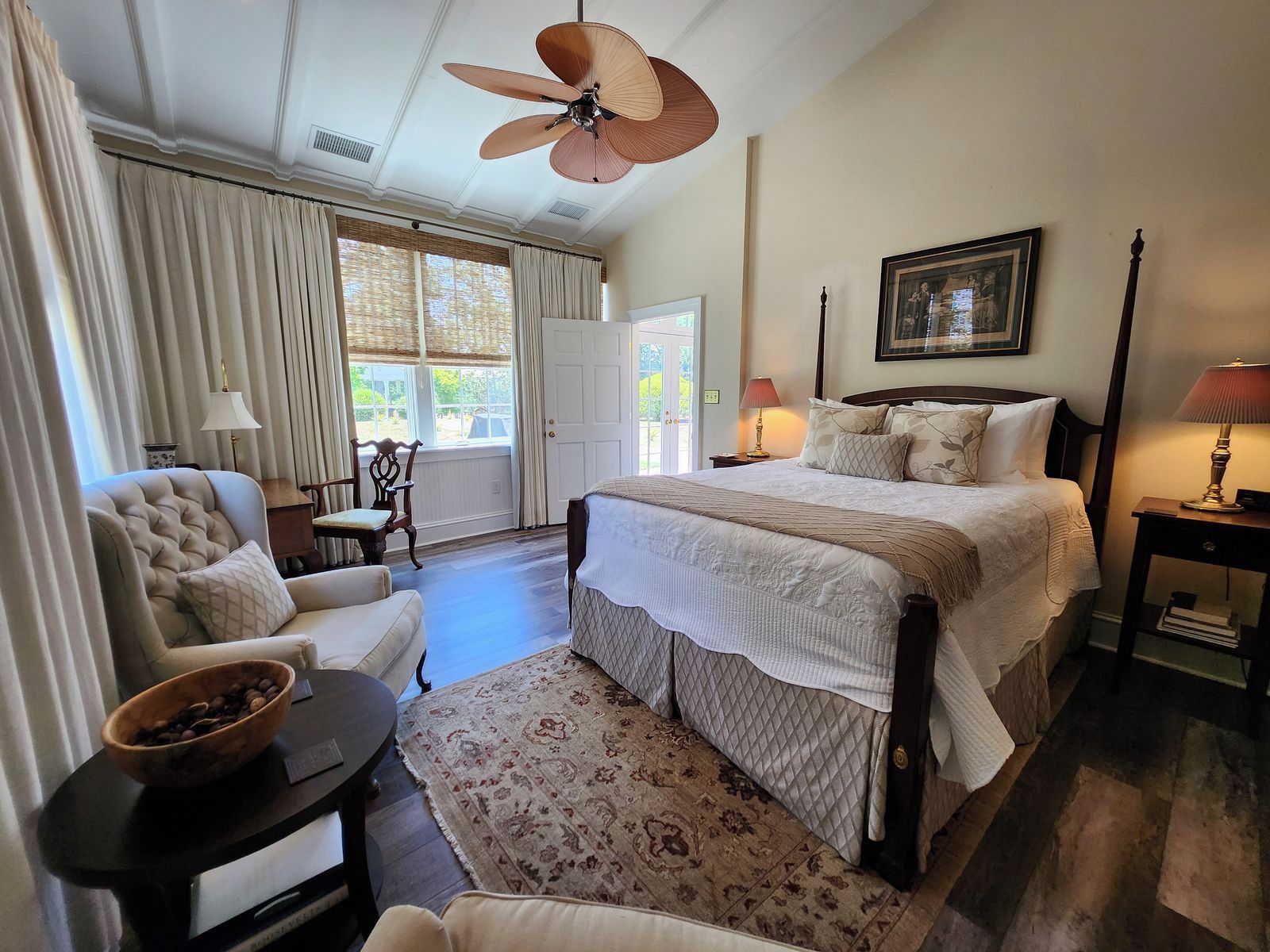 A bedroom with a bed, a chair, a table, a floor lamp, and a ceiling fan.
