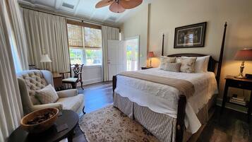 A bedroom with a bed, a chair, a table, a floor lamp, and a ceiling fan.
