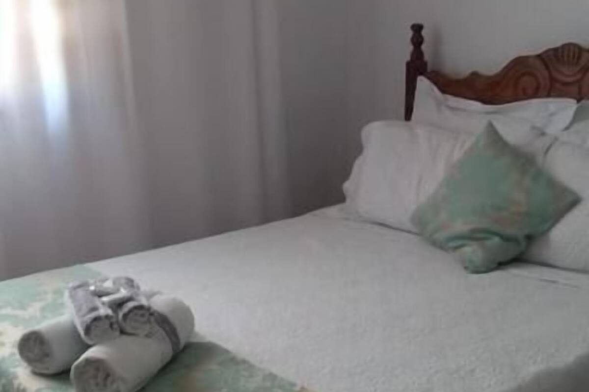 A neatly made bed with a green and white bedspread, a pair of rolled towels, and a wooden headboard.