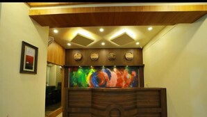 A reception desk with a wooden finish and a colorful abstract painting above it. - White Gate Luxury Hotel (Iritty)