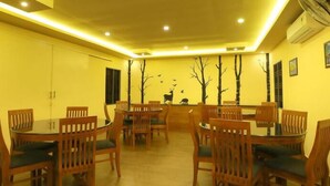 A dining area with round tables and wooden chairs, recessed ceiling lighting, and wall-mounted air conditioning units. - White Gate Luxury Hotel (Iritty)