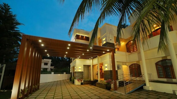 A modern building with a covered entrance, a staircase, and a well-lit outdoor area with palm trees. - White Gate Luxury Hotel (Iritty)