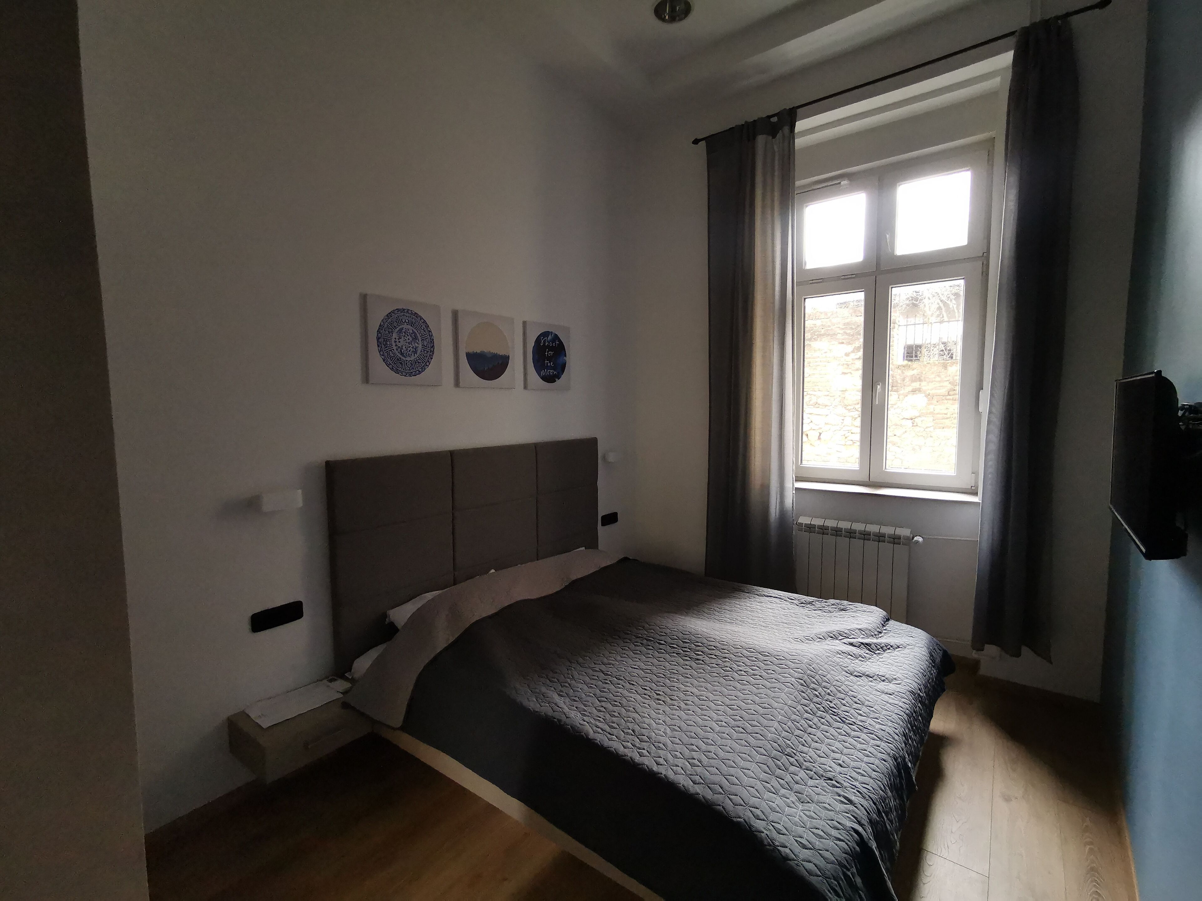 A bedroom with a bed, a window with curtains, and three wall-mounted artworks.