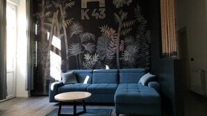 Una sala de estar moderna con un sofá azul oscuro, una mesa de centro redonda de madera y un mural con follaje tropical y letras.