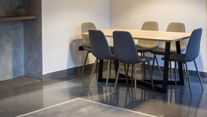 Un comedor moderno con una mesa redonda, seis sillas, una lámpara colgante y un estante en la pared con objetos decorativos.