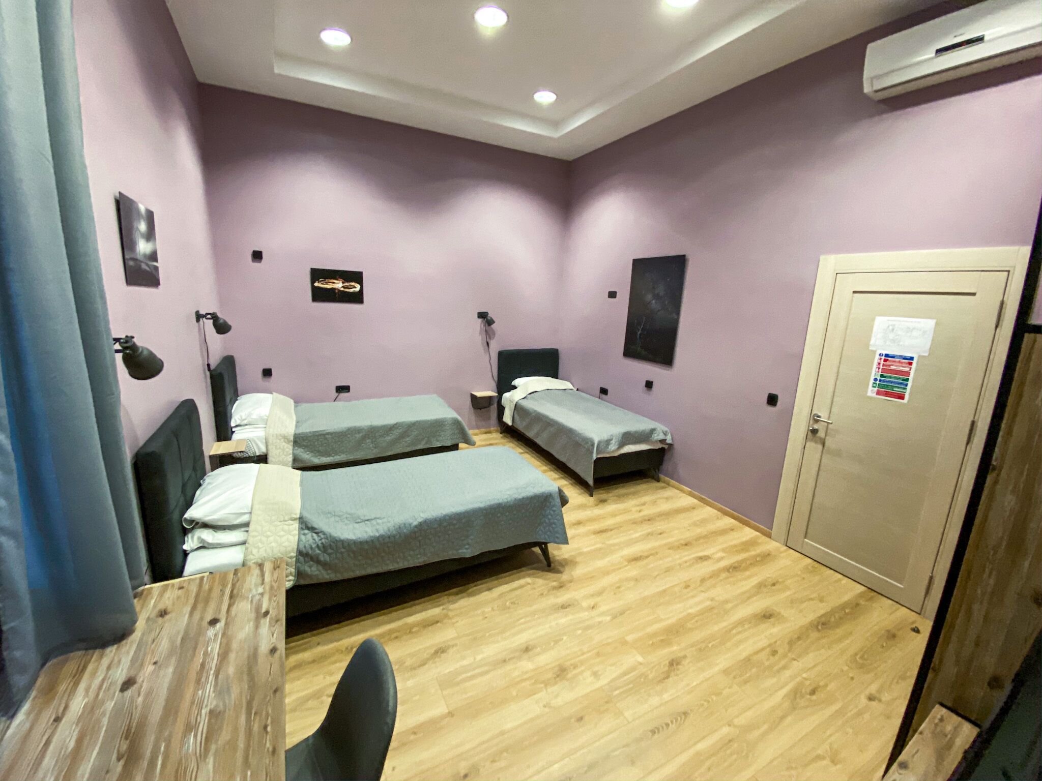 A room with two single beds, a wooden desk, a chair, a desk lamp, and an air conditioning unit.